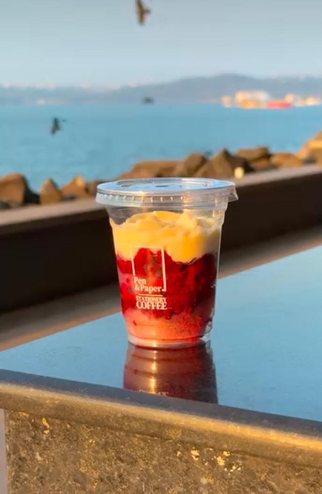 A red velvet dessert cup layered with cream, on a ledge overlooking the sea.